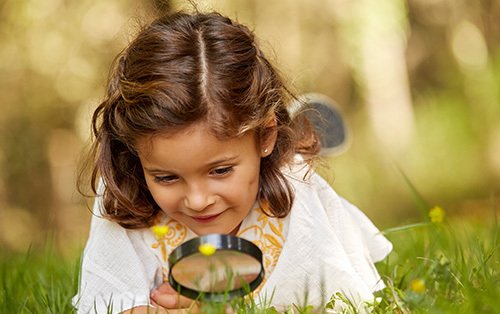 Girl looking at grass through magnifying glass